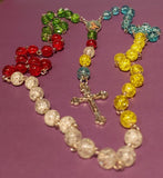 Each decade depicts a region. Blue decade represents the ocean around the Pacific Islands, yellow decade represents the morning light of the East for Asia, the white decade symbolizing Europe, the seat of the Holy Father, shepherd of the world, the red decade representing the calling to mind of the fire of faith that brought missionaries to the Americas and the green decade represents the forests and grasslands of Africa. Kim Williams Patenôtrier Rosaries, The Village Artist, Proudly South African.